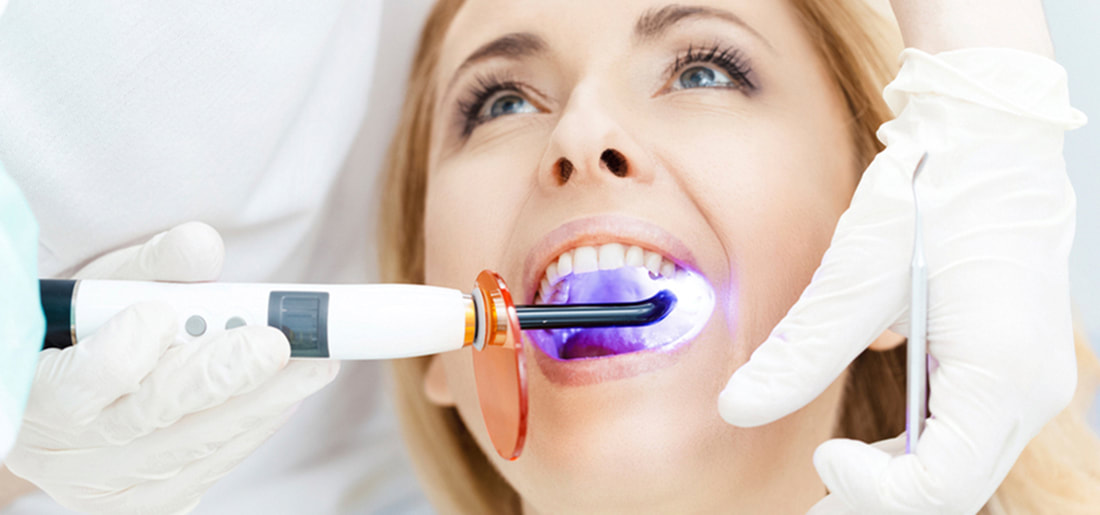 Teeth Whitening - Female dentist giving laser treatment to patient.