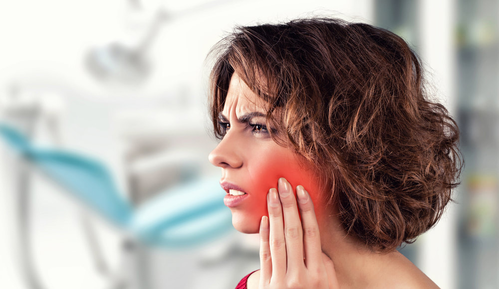 ​Preventative Dentistry - Woman with hand on the side of her cheek in pain. 